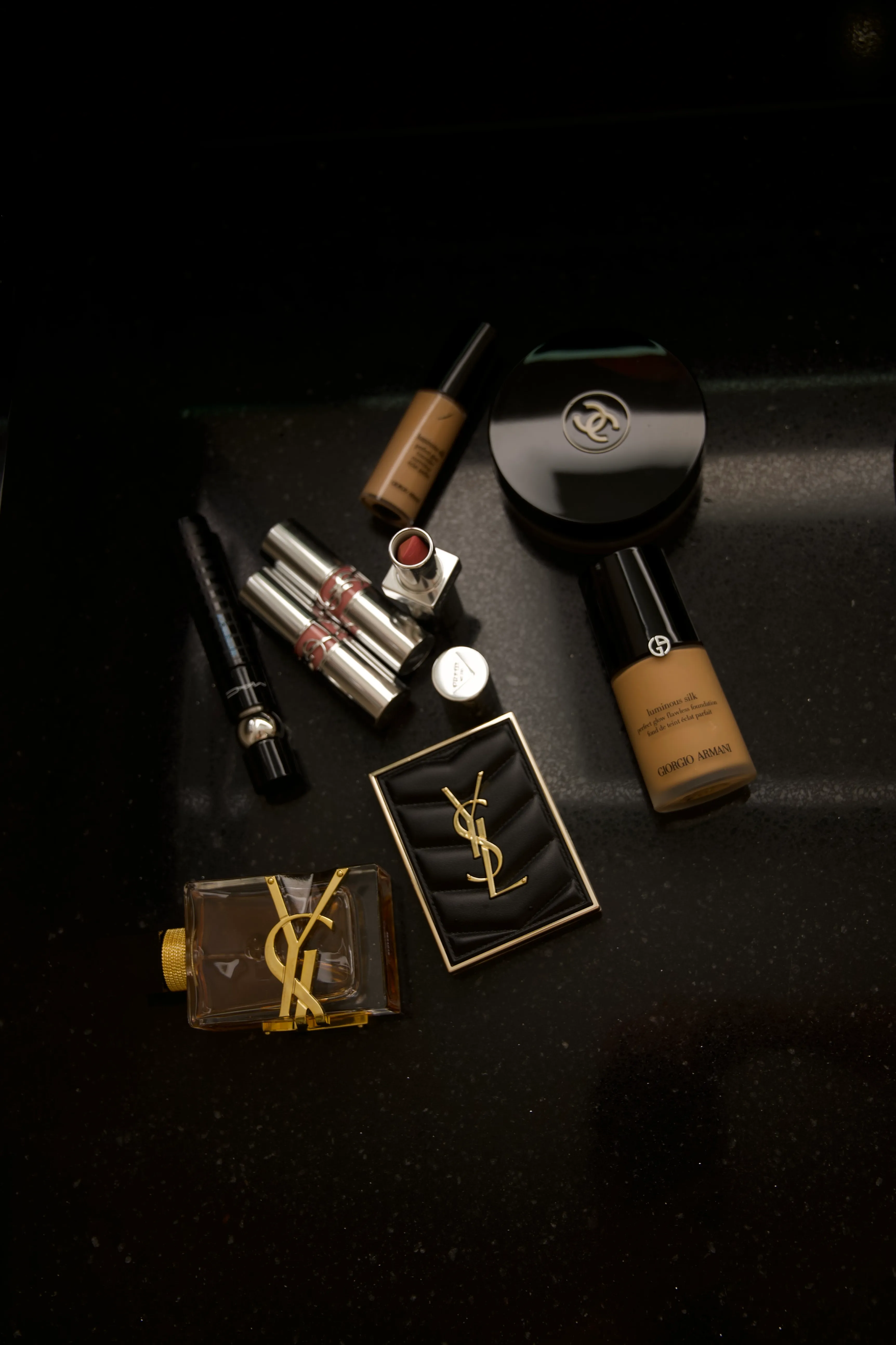 Luxury makeup and fragrance products arranged on a dark surface