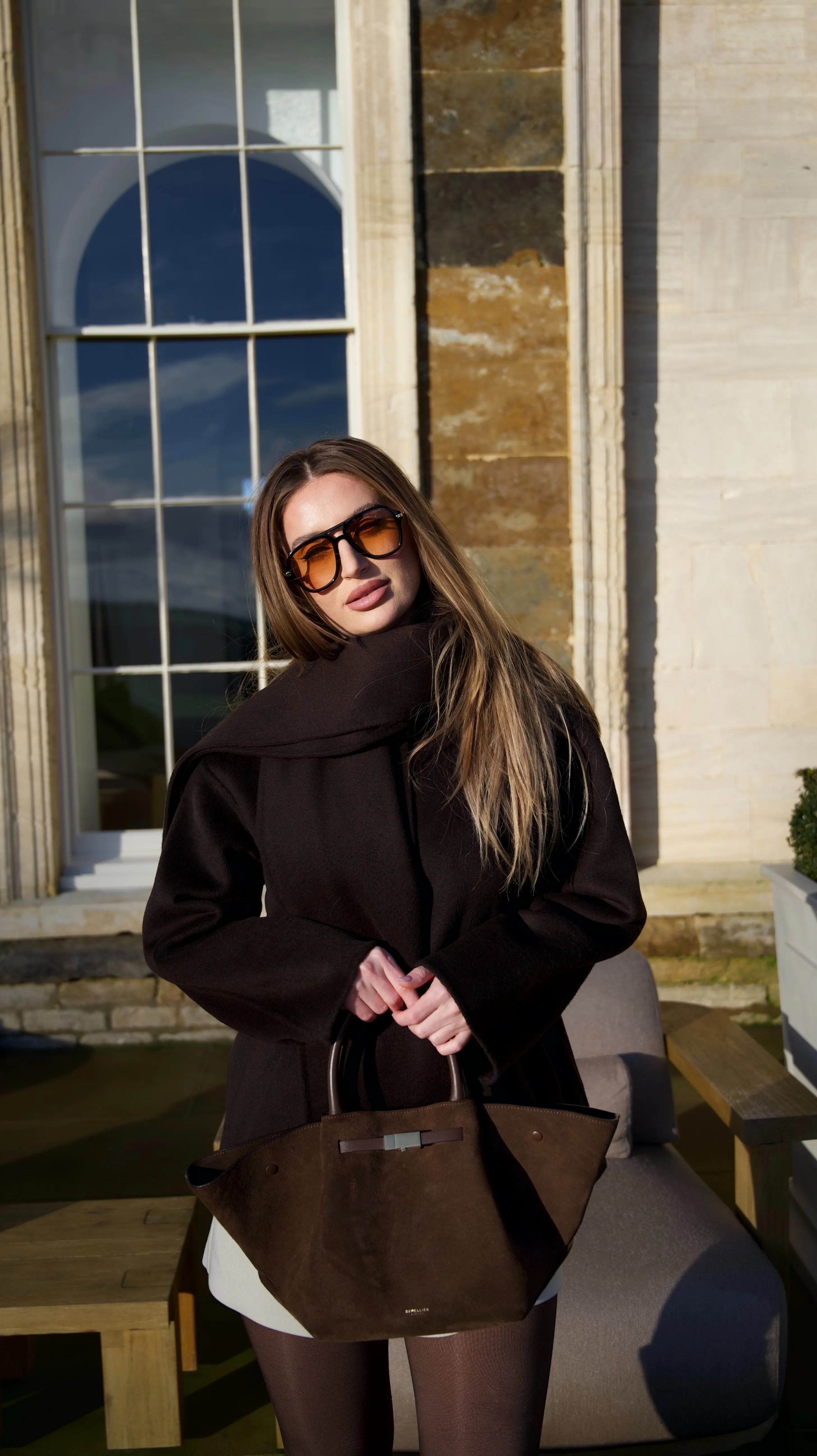 Valentina Fanu wearing sunglasses and a dark coat, holding a brown handbag