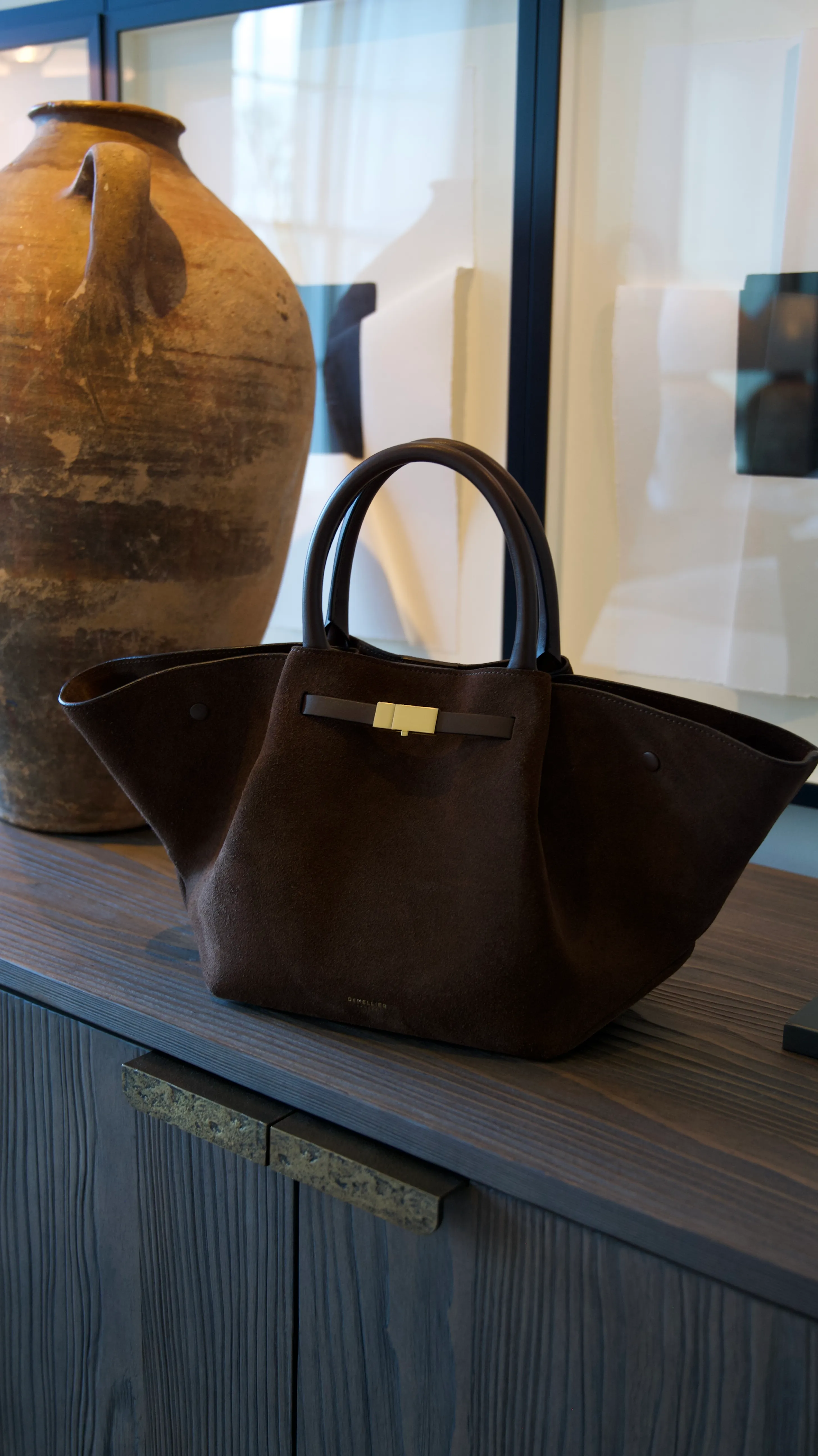 Chocolate brown Demellier handbag displayed on a shelf